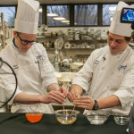 Culinary arts technology student Alex P. Korbich, of Sunbury, left, and culinary arts and systems student Paul R. Herceg, of Chalfont, drop orange soda that has been mixed with sodium alginate into a water/calcium chloride solution to cause “spherification” – resulting in tiny, caviar-like balls …