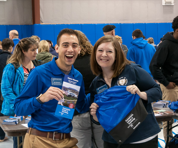 Ambassador Ryan Monteleone and Mallory L. Weymer, coordinator of student health and wellness education/suicide prevention specialist, playfully show off essential Open House swag: an activity guide and a convenient carry-all for information gathered throughout the day.