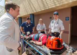 During a three-day set of emergency simulations that involved 320 Penn College students, Timothy F. Schwartzer (in hat), an emergency medical services student from Bensalem, explains to students in other health sciences majors how paramedics would begin treatment for a patient – played by a volunteer actor – who had fallen from a second-floor balcony.