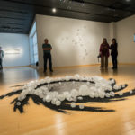 An 8-foot circle of acrylic on translucent Plexiglas and sand decorates the gallery floor. Titled “Full Circle,” the work inspired the exhibit’s name.
