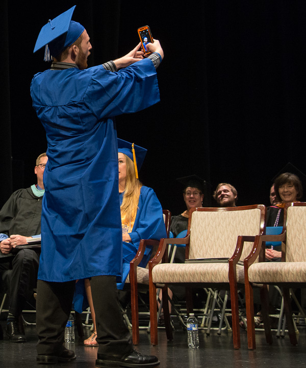 As he makes his way across the stage, a graduate pauses for a selfie with the audience as background. 
