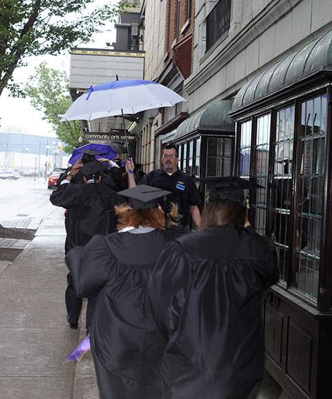 As rain falls during the Saturday afternoon procession, College Store manager Matt Branca is among those providing helpful shelter for the half-block sprint.