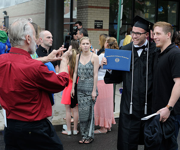 Accustomed to being on the other side of a camera, former student photographer Caleb G. Schirmer, who earned a bachelor's degree in applied management, is snapped by his father, George L. At right is friend Kyle J. Eccher, a December 2014 graduate in aviation maintenance technology.