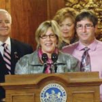 Backed by her husband, Greg, right, and former Gov. Tom Corbett, Spinello speaks at the signing of the Pennsylvania Breast Density Notification Act.