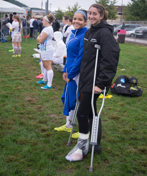 With an injured ankle wrapped in plastic, Francesca M. Timpone and soccer teammate Tania Parra smile through a damp and muddy day. 