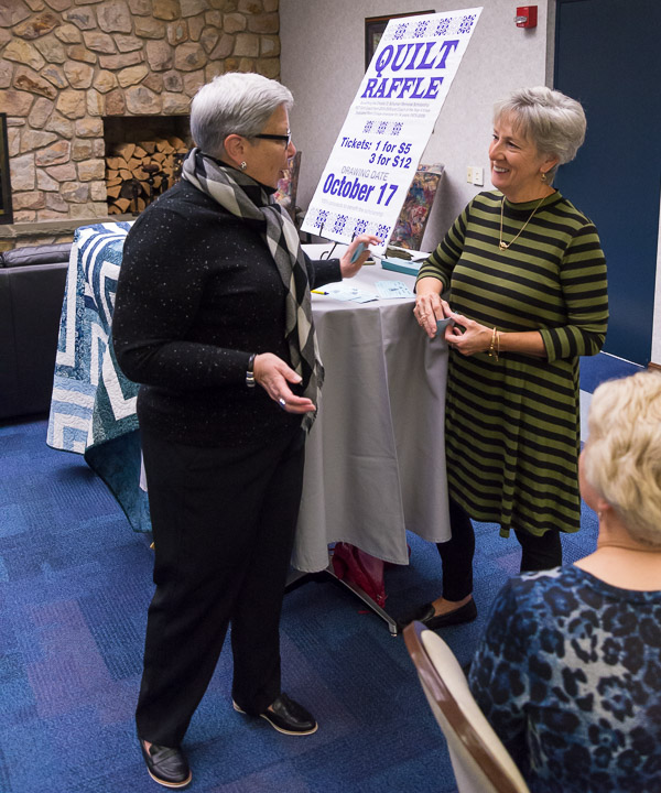 The president talks with Pam Schuman, whose late husband, Chester D., was the college's longtime admissions director and golf coach. A quilt is being raffled to raise money for a memorial scholarship fund.