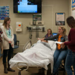 In the Nursing Education Center, guests attend a simulated delivery under the guidance of Jessica L. Bower (at bedside), simulation laboratory coordinator, and Samantha M. Weaver, (background) learning laboratory coordinator.