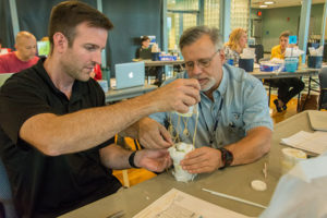 Keith Cremer, left, an eighth-grade science teacher in the South Williamsport Area School District, and Dan Zerbe, who teaches STEM and other courses in the East Lycoming School District, strategize to use the materials on hand to slow down the vessel that they’ve designed to carry an egg from a second-floor balcony to the ground level.