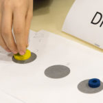 In a “Coding Unplugged” session, a student solves a problem by moving disks from one spot to another. Students learned that repeating and combining the movements that solve a simple problem can solve more complex problems.