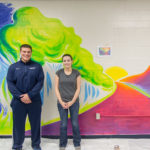 John M. Arrigonie, lab supervisor for exercise science, and artist Lindsey Martin pause in front of the in-progress mural, which was completed between Finals Week and Winter Break.
