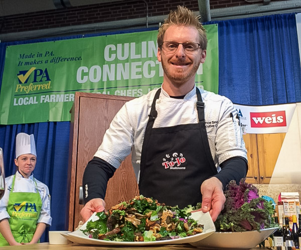 Chef Lance Smith, who earned a bachelor’s degree in culinary arts technology from Penn College in 2006, demonstrates warm mushroom and kale salad with pickled mustard seeds and a smoked walnut vinaigrette. He is executive chef of The Millworks in Harrisburg. His on-stage assistants were Danielle M. McGuire (background) and Tessa M. Stambaugh.
