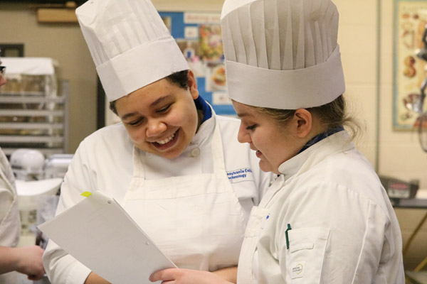 Baking and pastry arts students Ariana M. Bauer, of Coburn, and Nora E. Smith, of Centre Hall, look over a formula – one of 54 students prepared for the dinner’s dessert reception.