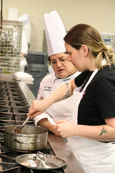 Gardner consults with her former instructor, Chef Mary G. Trometter, assistant professor of hospitality management/culinary arts, who helped her to lead students in preparing hummus, pitas and salatim for the pre-dinner reception.