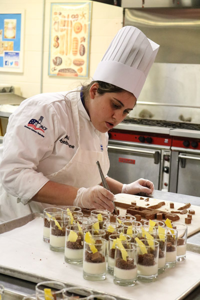 Baking and pastry arts student Ally T. Monborne uses tweezers to carefully place a chocolate-peanut butter morsel into one of the dessert offerings.