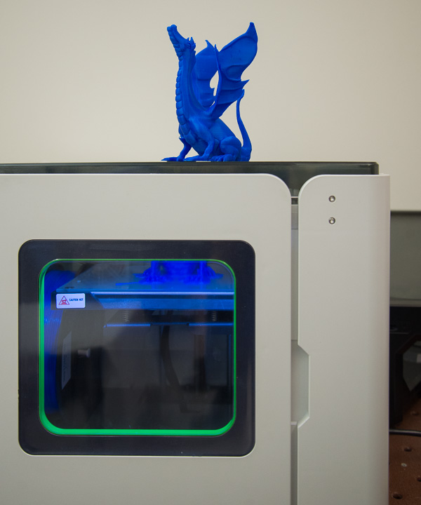 In additive manufacturing, a prototype sits atop a printer while another 3-D model of a blue dragon takes shape inside.