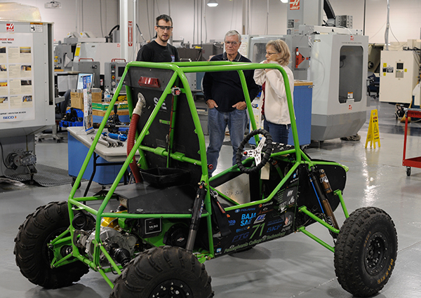 Manufacturing engineering technology student Jonathan R. Sutcliffe, of Orangeville, a member of the college’s SAE Baja team, talks with John and Dee Hobrle beside the vehicle in CAL's automated manufacturing lab.