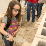 With a work ethic befitting her T-shirt (which reads “Try to Keep Up”) a girl lays brick after brick.