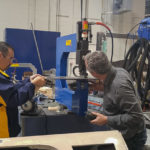 Roy H. Klinger (right), instructor of collision repair, provides a hands-on lesson on the louver press, used to make hood vents.
