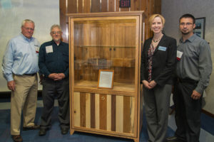 Showcasing a display case constructed of Pennsylvania lumber are, from left, Don Remmey, the business owner who donated the piece to Penn College; Abe Weaver, the woodworker who crafted it; Elizabeth A. Biddle, the college’s director of corporate relations; and Erich R. Doebler, laboratory assistant for forest technology at the college.
