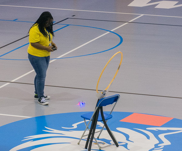During an end-of-week showcase, a girl maneuvers her quadcopter toward an obstacle.