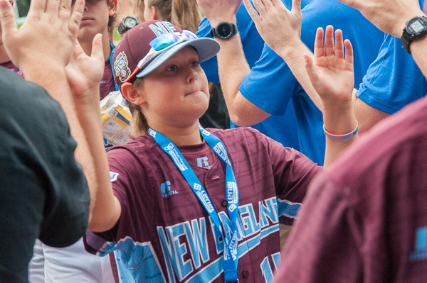 A New England player from Fairfield (Conn.) American Little League accepts high fives from the right and left.