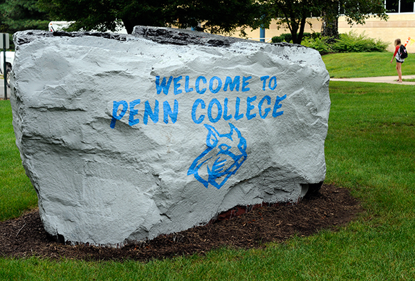 A student walks alongside the Advanced Technology & Health Sciences Center, near an open-arms message on The Rock.