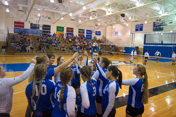 Volleyball coaches and players huddle before the start of play.