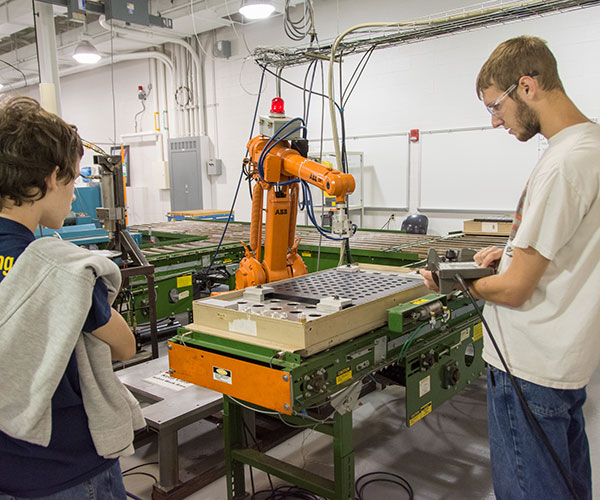 Automated manufacturing technology student Aren T. Way (right) of Jersey Shore, demonstrates an industrial-scale robot during a session on “Industrial Robotics, Hydraulics and Pneumatics, and CNC Machine Tools.”