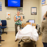 School nurses visit SimMom, a high-fidelity manikin that has a pulse, breathes, talks and has contractions as she delivers a manikin baby. Several served as delivery nurses in a simulation coordinated by Jessica L. Bower (center), simulation laboratory coordinator.