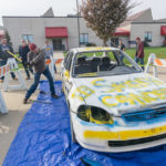 With safety precautions in place – a tarp, protective goggles, removal of glass and fluids – a participant adds his mighty two cents (and then some).