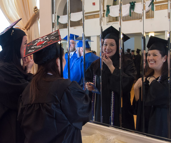In the Genetti Hotel ballroom that serves as a staging area, nursing graduates Danielle N. Dent (left) and Francesca B. Monse make final adjustments in a conveniently placed mirror.