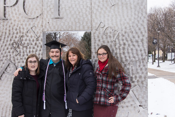 Timothy M. Kainzbauer, a new information technology sciences-gaming and simulation graduate from Mifflinburg, takes a photo with his family in front of a silver landmark that fits the campus’s winter wonderland.
