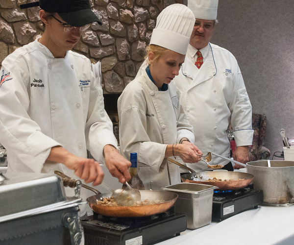 Chef Paul Mach, assistant professor of hospitality management/culinary arts, leads students Jacob W. Parobek and Ashley R. Potrzebowski in a live demonstration of osso buco for Food Show visitors. 