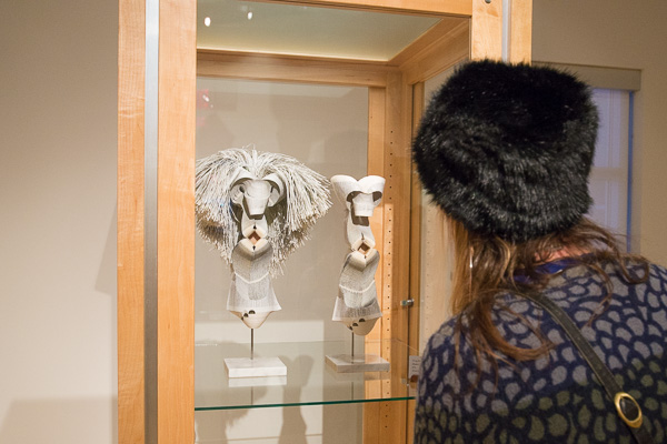 A gallery-goer peers into a glass case displaying Beube’s “Masked Wisdom & Masked Erudition.” 