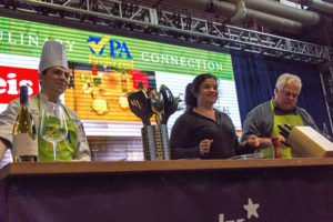 At the 2018 Farm Show, Penn College student Paul J. Herceg, of Chalfont, provides on-stage assistance to Food Network star Chef Alex Guarnaschelli (center), who is also accompanied by mushroom farmer David Santucci as she demonstrates her recipe for broiled cauliflower steaks. Herceg is pursuing a bachelor’s degree in culinary arts and systems.