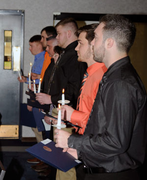 Their candles carrying the light of knowledge, inductees return to their seats amid recognition from the audience.