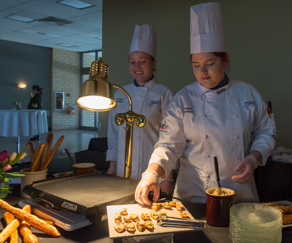 During the pre-dinner reception, Bridget M. Callahan, of Pottsville, and Somer A. Safford, of Port Allegany, grill slices of student-baked crostini and top them with Stinky Pimento Cheese.