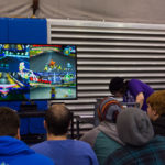 A group of students watches as four players race one another for first place in Mario Kart.