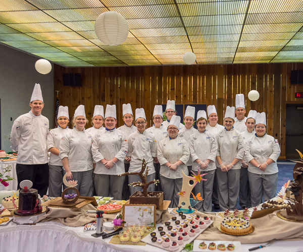 Students in the Pastry Food Show and Buffet Presentation Concepts course, which presents the Grand Pastry Buffet, take a pre-event photo with two of their faculty members: Chef Charles R. Niedermyer, (left) and Chef Todd M. Keeley, instructors of baking and pastry arts/culinary arts.