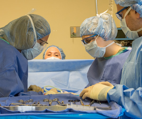 While classmates from other disciplines watch live on a big screen outside the simulated operating room, surgical technology students act out a surgical procedure.