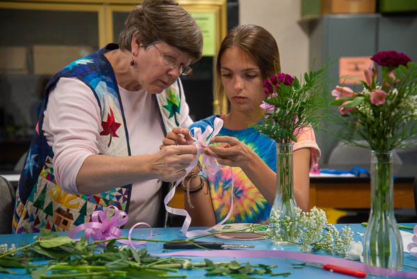 Karen R. Ruhl, a part-time horticulture faculty member and alumna, aids a camper in assembling a bow from ribbon. 