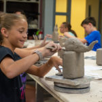A camper delights in her clay creation: an elephant-inspired bee house. When complete, campers can place their bee houses outside their homes to enhance bee habitat. 