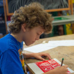 Penn College art studios offer welcoming space for artistic expression and exploration. Here, a young camper adds finishing touches to his creation in a printmaking workshop.