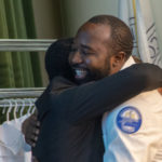 Katanga Muanza, of Williamsport, hugs Emil Lukasa after receiving his white coat and pin.