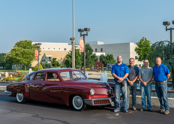 Some members of the Tucker restoration team gather at Penn College’s main entrance for the vehicle’s celebratory sendoff to California. From left are Weigle and faculty members Klinger, Christopher H. Van Stavoren and Vlacich.
