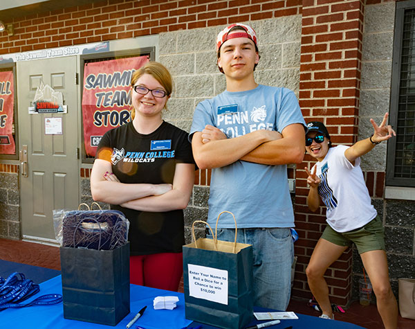 Staffing a table are student workers Cas D. Henderson, of Hazel Hurst, and Jacob T. Bowers, of Shippensburg – photobombed with enthusiasm by Cathy E. Gamez, resident hall coordinator.