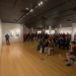 A large crowd listens intently to the artist’s stories.