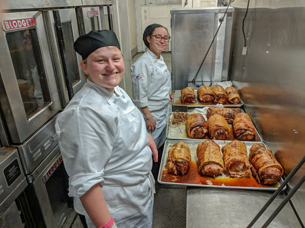 Baking and pastry arts students Sadie C. Bower (left), of Lewisberry, and Olivia M. Lunger, of Elysburg, pull roasted pork loin from a long line of convection ovens.