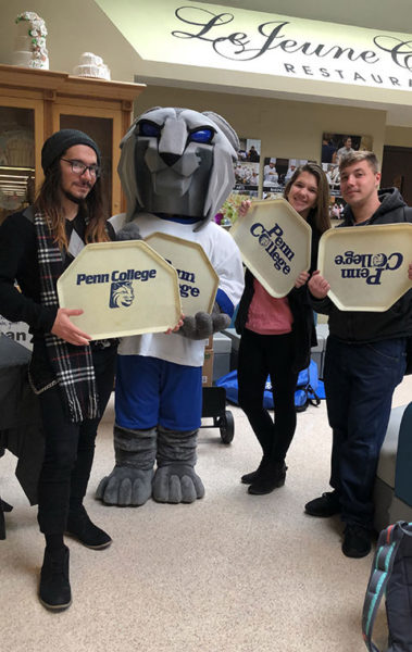 Students join the Penn College Wildcat in the “One Tray at a Time” benefit, during which the campus community loaded vintage cafeteria trays with nonperishables for The Cupboard. From left are Perry R. Leslie Wheat, a graphic design major from Millheim; Jordan M. Scott, of Cogan Station, enrolled in residential construction technology and management: building construction technology concentration; and Kory J. Zielinski, a manufacturing engineering technology student from Honesdale.