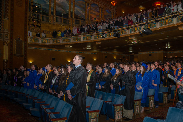 Riley H. Hengler (foreground), of South Williamsport, who received a bachelor's in accounting, rises with classmates and guests ...